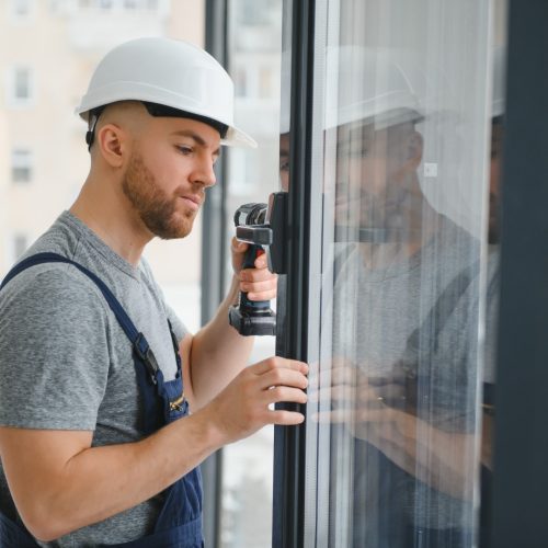 Workman in overalls installing or adjusting plastic windows in the living room at home تركيب ابواب وشبابيك